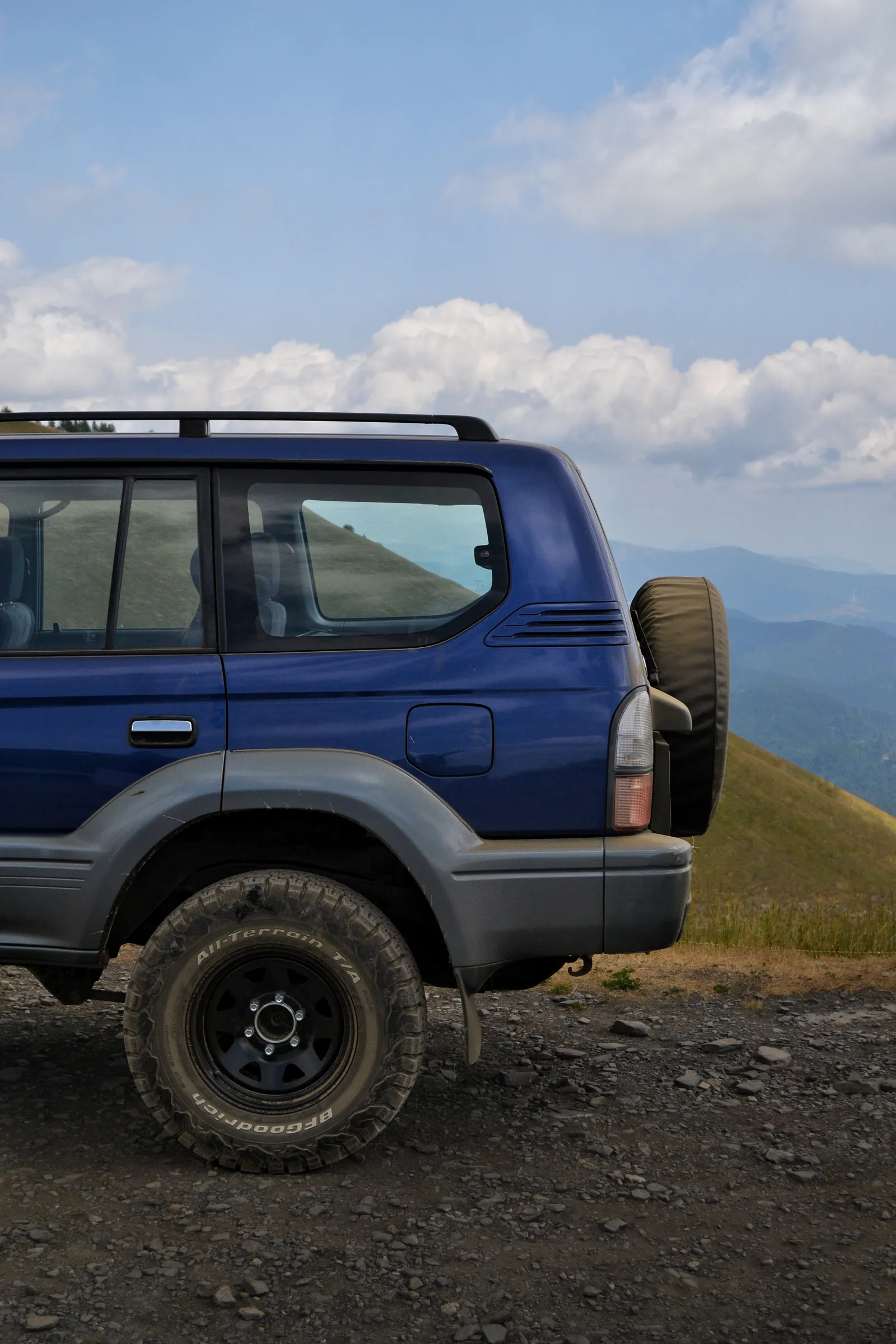 Blue off-road SUV with a rear spare wheel on a mountain track