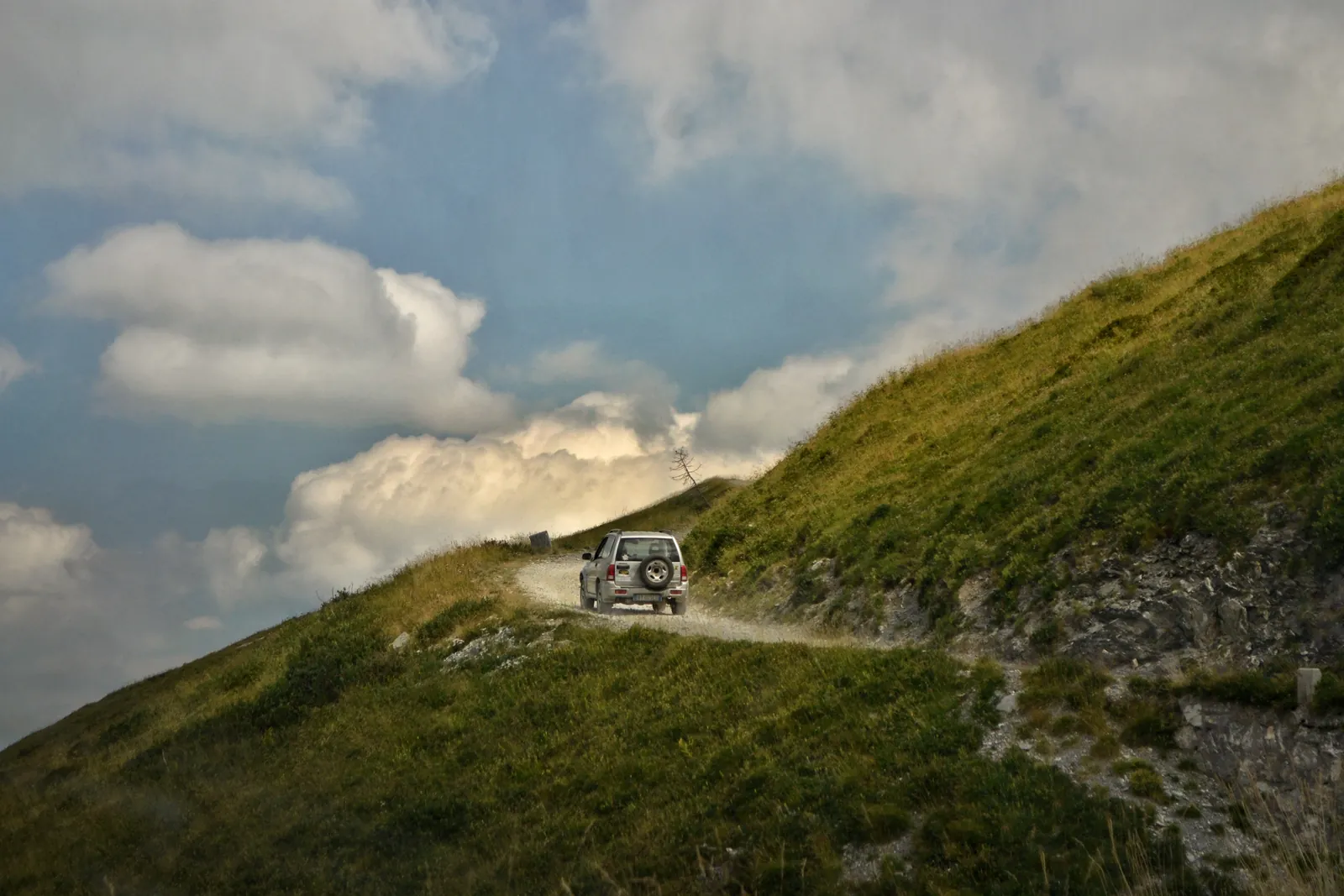 Off-road vehicle climbing a grassy mountain track under a cloudy sky