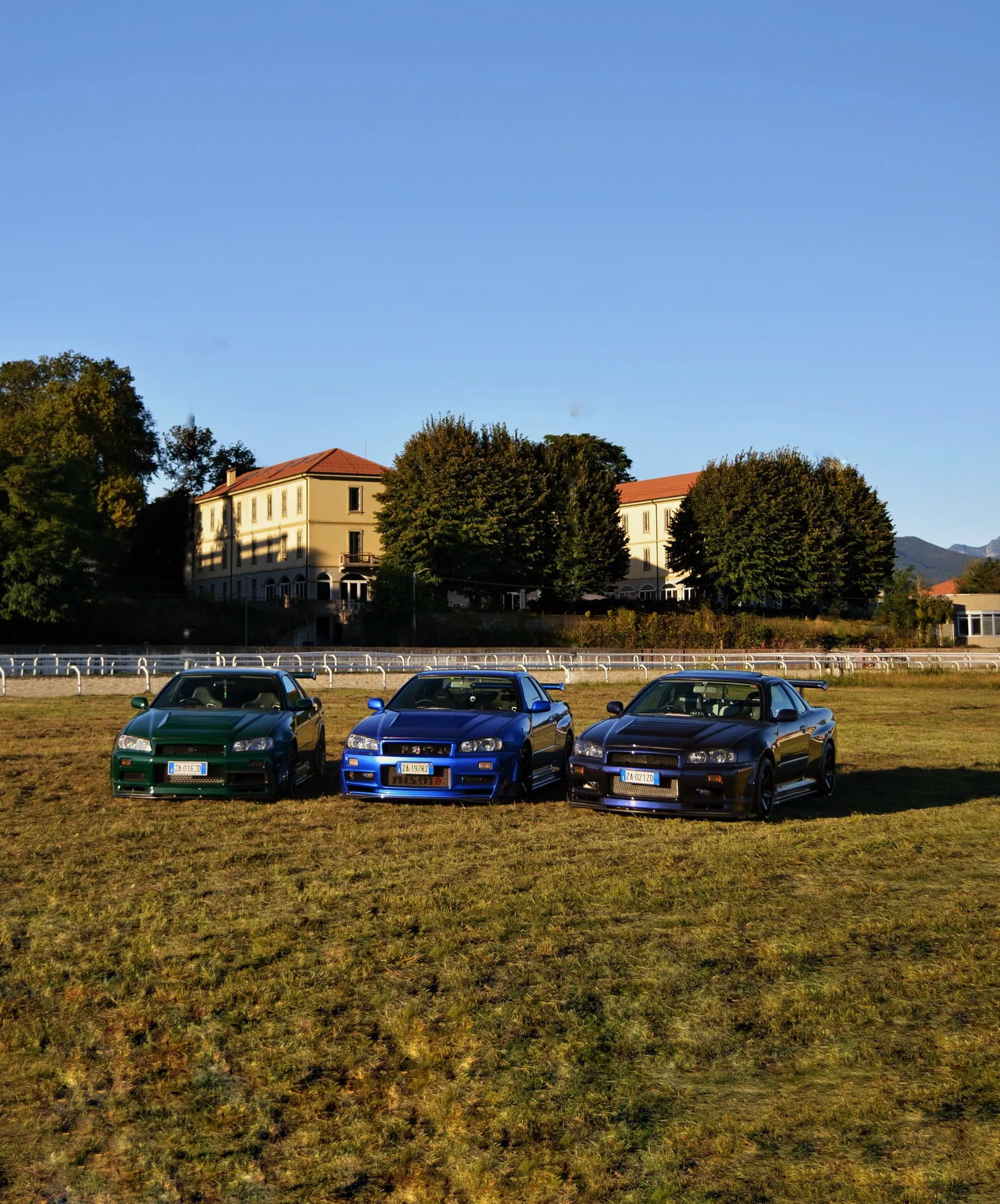 Three Nissan Skyline GT-R parked on a field in front of a villa