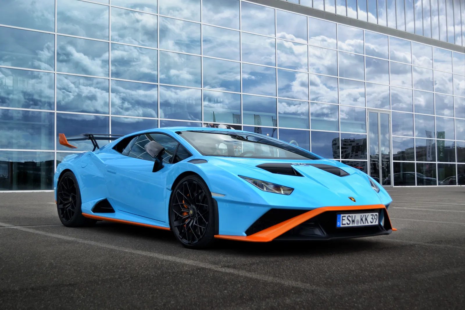 Light blue Lamborghini Huracán STO with orange details in front of a glass building
